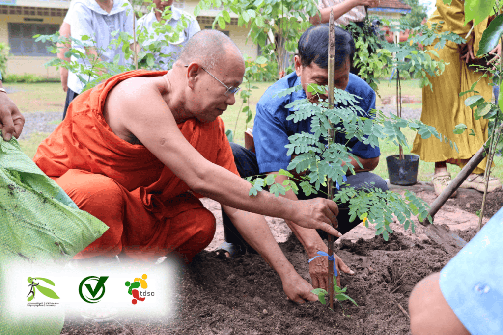TDSO Monk and community members planting a young tree outdoors.